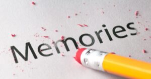 Close-up of the word 'Memories' on paper with red eraser shavings scattered around, suggesting erasing memories.