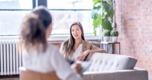 - Treat Mental Health California Two women in a modern office conversing; one sits on a gray sofa and speaks while the other listens from the foreground.