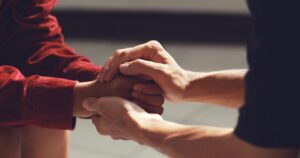 - Treat Mental Health California Close-up of two people in a comforting grip, hands clasped around each other's wrists. One person wears a red sleeve.