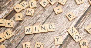 Scrabble tiles on a wooden surface spelling the word MIND with surrounding letters scattered.