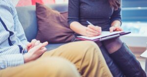- Treat Mental Health California Two people sit on a sofa; one writes on a clipboard while the other rests hands in a casual setting.