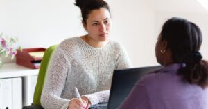 - Treat Mental Health California Two women in an office discuss a document: one writes in a notebook while the other looks on at a laptop.