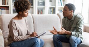 - Treat Mental Health California Two adults sit on a beige sofa in a bright living room; one writes in a notebook while the other speaks with openhanded gestures.