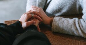 - Treat Mental Health California Two people clasping hands on a wooden table, showing care and support.