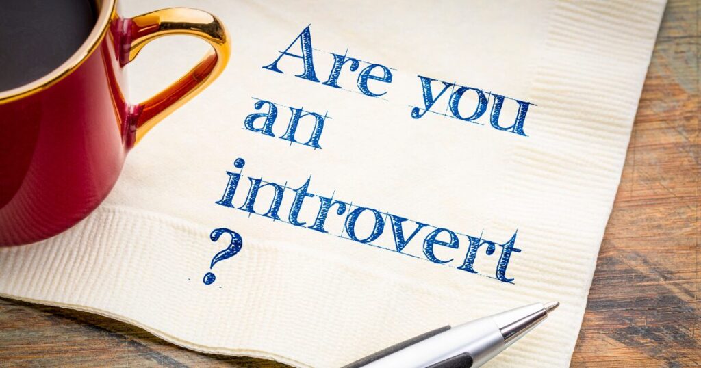 Napkin with blue stamped text reading 'Are you an introvert?' beside a red mug and a pen on a wooden table.