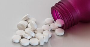 White round tablets spilled from a pink bottle onto a light surface, suggesting medication.