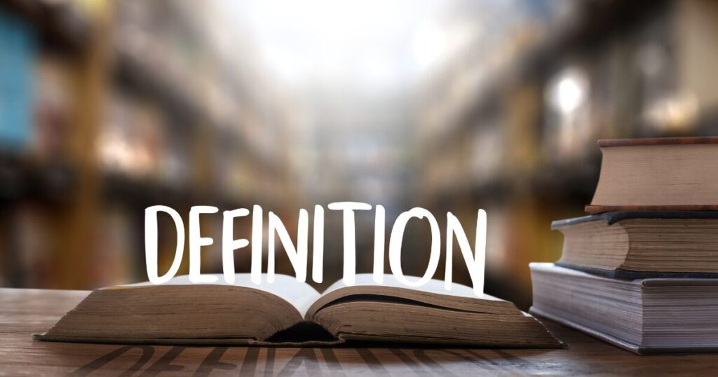 Open book on a wooden table in a library with a stack of books to the right and the word DEFINITION across the page.