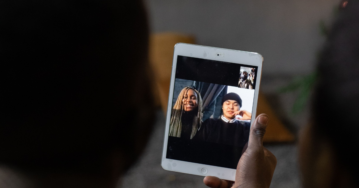 Person holds a tablet displaying a video call with two smiling friends on screen.