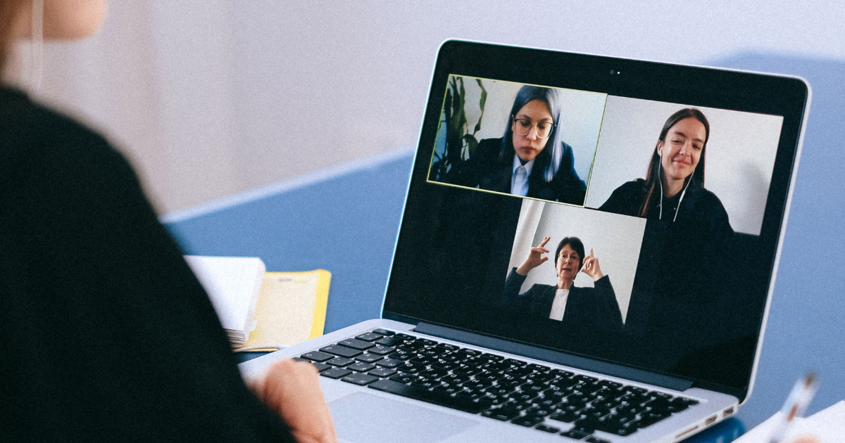 Person wearing headphones typing on a laptop during a video conference with three participants on screen.
